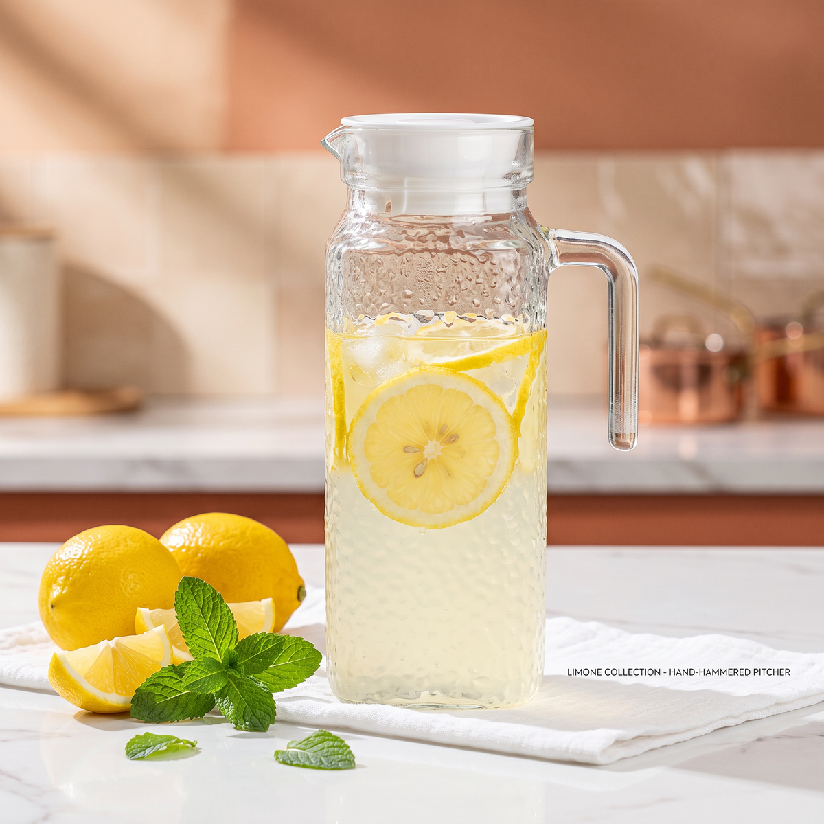 Jarra de vidrio martillada con limonada y limones en mesón de cocina